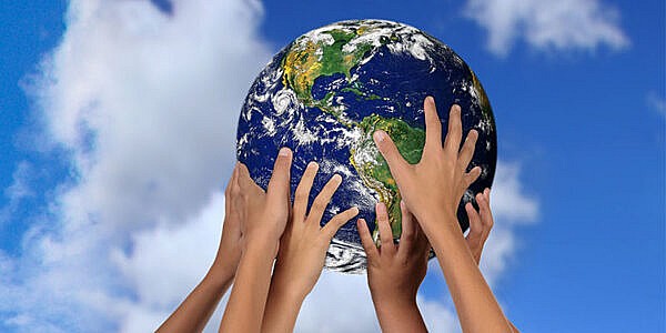 hands holding up a globe against background of blue sky and clouds