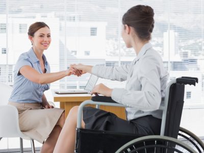 Photo showing businesswoman shaking hands with colleague in a wheelchair
